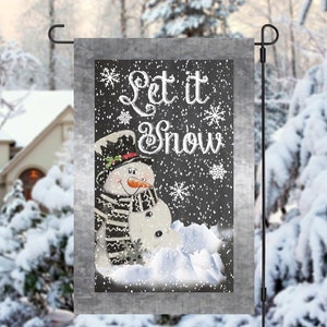 May include: A winter-themed garden flag with a snowman and the text "Let it Snow" on a black chalkboard background. The flag is decorated with white snowflakes.