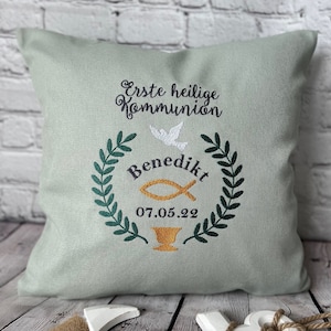 Puede incluir: Una almohada verde claro con texto bordado que dice "Erste heilige Kommunion" y "Benedikt" con una fecha de "07.05.22" y un diseño de paloma y pez.