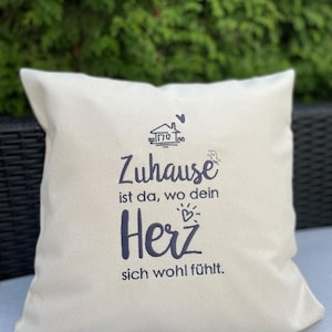Könnte beinhalten: Ein weißes Kissen mit schwarzer Stickerei, auf dem "Zuhause ist da, wo dein Herz sich wohl fühlt." steht. Das bedeutet "Zuhause ist da, wo sich dein Herz wohlfühlt."