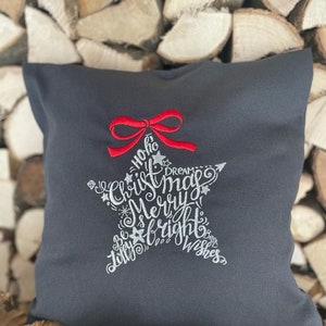 May include: A grey throw pillow with a white embroidered star featuring the text "Yo ho ho Christmas Dreams Merry & Bright Jolly Best Wishes". A red bow is at the top of the star.