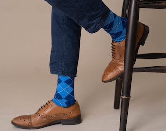 May include: A person wearing blue jeans and brown leather shoes with blue and white patterned socks. The person is sitting on a wooden stool.