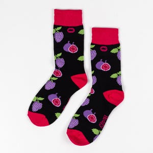 Puede incluir: Calcetines negros con puños, talones y punteras rojos, estampados con uvas moradas e higos. Los calcetines tienen el nombre de la marca "Hedgy" impreso en el lateral. No hay medidas disponibles.