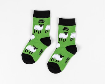 May include: A pair of green socks with a black sheep pattern. The socks have black cuffs and the words "Socks" are printed on the bottom of each sock.