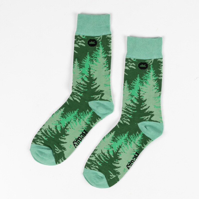 May include: A pair of green and light green socks with a forest print. The socks have a black logo that says "Hewey" on the bottom of each sock.