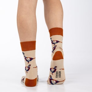 May include: A pair of beige socks with a brown pheasant print. The socks have a brown cuff and the text "HEDGY SOCKS" is printed on the back of one sock.