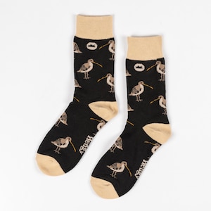 May include: A pair of black socks with a beige cuff. The socks feature a repeating pattern of brown birds with long beaks on a black background. The socks have the word "Hewey" printed on the bottom of each sock.
