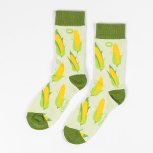 Peut inclure: Une paire de chaussettes vertes et blanches avec un motif d'épis de maïs. Les chaussettes ont un revers vert et un fond blanc avec du maïs jaune sur l'épi.