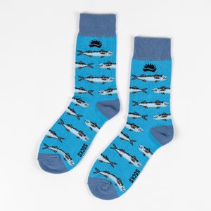 Könnte beinhalten: Ein Paar blaue Socken mit einem sich wiederholenden Muster aus weißen Fischen. Die Socken haben hellblaue Bündchen, Fersen und Zehen. Das Wort "SOCKS" ist auf der Seite jeder Socke aufgedruckt.