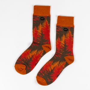 May include: A pair of orange and red socks with a forest print. The socks have a brown cuff and a small black logo on the cuff.