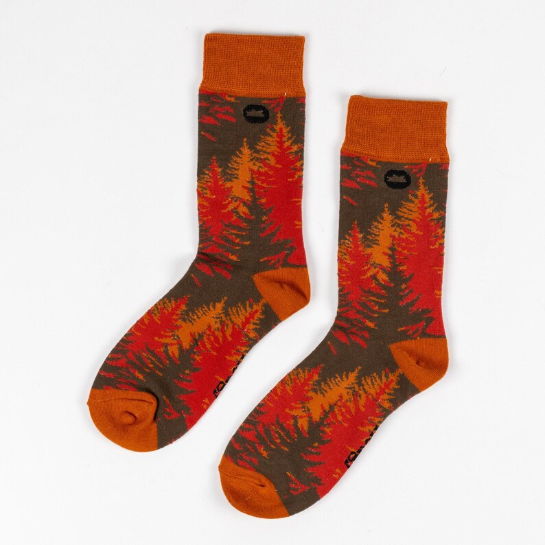 May include: A pair of orange and red socks with a forest print. The socks have a brown cuff and a small black logo on the cuff.
