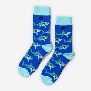 May include: A pair of blue socks featuring a repeating pattern of cartoon sharks in grey and white. The socks have light blue heels, toes, and cuffs, and a small black crown logo near the cuff.