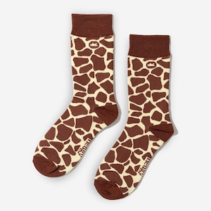 May include: A pair of crew socks with a giraffe pattern. The socks feature a brown and cream-colored design, with brown cuffs, heels, and toes. The brand name "negy" is printed on the side of each sock.