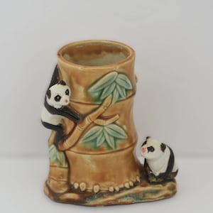 May include: A ceramic panda bear planter with a bamboo design. The planter is brown with green leaves and features two panda bear figurines, one climbing and one sitting. The planter is approximately 6 inches tall.