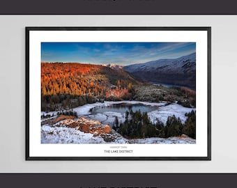 May include: Framed print of Harrop Tarn in the Lake District. The landscape features a lake surrounded by snow-covered ground and trees. The sky is blue with a hint of orange and pink from the sunrise. The text "HARROP TARN" and "LAKE DISTRICT" are displayed.