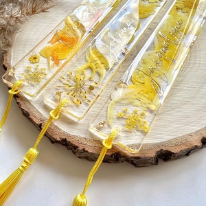 Pu&ograve; includere: Quattro segnalibri in resina gialla con fiori pressati e lettere dorate. I segnalibri hanno nappe gialle.
