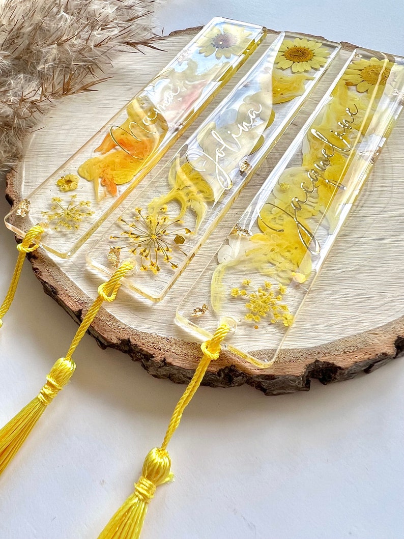 Pu&ograve; includere: Quattro segnalibri in resina gialla con fiori pressati e lettere dorate. I segnalibri hanno nappe gialle.