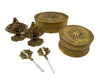 May include: A set of vintage gold-toned vanity items, including two ornate perfume bottles with glass applicators, and two round, intricately designed boxes with lids.