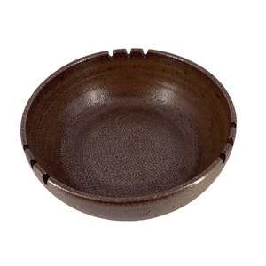 May include: A brown ceramic ashtray with a textured surface and four indentations around the rim.