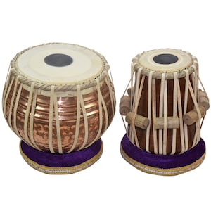 May include: A pair of traditional Indian tabla drums. The larger drum is made of copper and has a hammered finish. The smaller drum is made of wood and has a brown finish. Both drums have a purple velvet base.