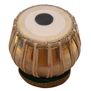 May include: A gold-colored tabla drum with a brown leather head and a black circle in the center. The drum is sitting on a green and gold base.