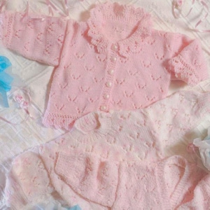 May include: Two pink knitted baby sweaters with delicate lace detailing. The top sweater has a button closure and a ruffled collar. The bottom sweater is a simple cardigan.