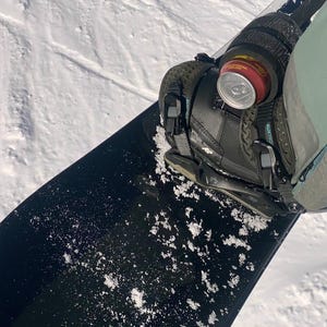May include: A black snowboard with a black binding and a can of soda attached to the binding.