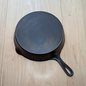 May include: Black cast iron skillet with a handle. The bottom of the skillet is marked with the text "Wagner Sidney O."