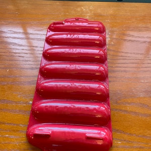 May include: Red metal baking dish with six individual molds for cooking sausages.