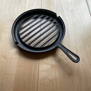 May include: Black cast iron grill pan with a round, ridged cooking surface and a long handle.