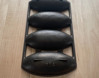 May include: Black cast iron bread pan with three oval-shaped moulds. The pan is labelled "No. 4".