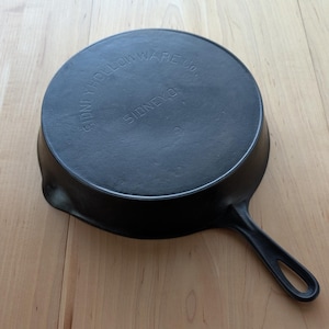May include: A black cast iron skillet with a handle. The bottom of the skillet is marked with the text "Sidney Hollow Ware Co., Sidney, O."