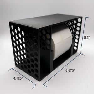 May include: Black label dispenser with a honeycomb pattern on the sides. The dispenser is 8.875 inches long, 5.5 inches high, and 4.125 inches wide. A roll of white labels is visible inside the dispenser.