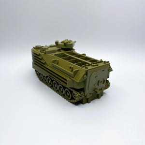 May include: A green plastic model of an amphibious assault vehicle with a raised turret and tracks. The vehicle has a cargo bed with open sides and a rear ramp.
