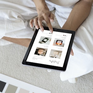 Puede incluir: Una persona usa una tableta que muestra una lista de productos. La pantalla muestra cuatro opciones de velas diferentes con varios envases y etiquetas. La palabra "Bestsellers" est&aacute; escrita en cursiva en la parte inferior de la pantalla. La persona est&aacute; sentada sobre una superficie blanca.