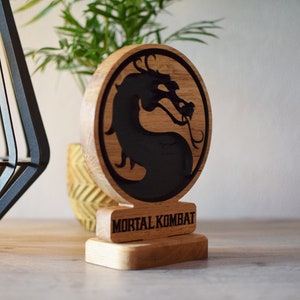 May include: A wooden stand with a black dragon logo and the words "Mortal Kombat" engraved on the front.