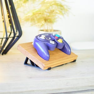 Op de afbeelding: Een paarse en grijze videogamecontroller staat op een houten standaard met een zwarte driehoekige basis.