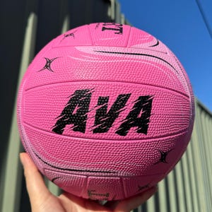 May include: Pink netball with black stitching and the name "AVA" printed in black on the side.