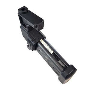 May include: Black airsoft magazine, angled, with a clear section showing white BBs. The magazine has a rectangular shape with a spring mechanism visible inside. The top has a small, angled section with a hole.