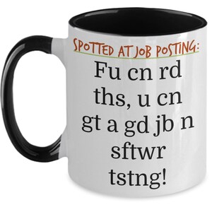 May include: White ceramic mug with a black handle and interior. The mug features the text "SPOTTED AT JOB POSTING: Fu cn rd ths, u cn gt a gd jb n sftwr tstng!" in black, with the words "SPOTTED AT JOB POSTING:" in green.