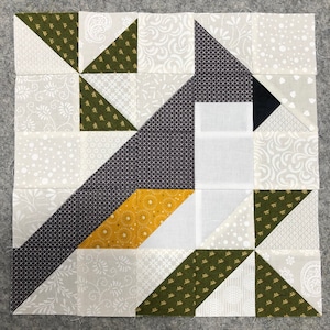 May include: A quilt block with a geometric design featuring a variety of fabrics in shades of gray, green, white, and yellow. The block is made up of squares and triangles, and the design is reminiscent of a bird.