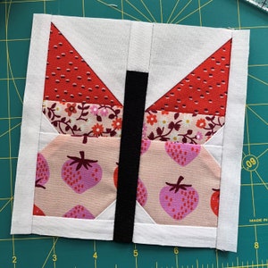 May include: A white fabric butterfly block with red, pink, and white patterned fabric. The butterfly has a black fabric body.
