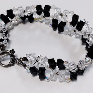 May include: A black and white crystal bracelet with a silver toggle clasp. The bracelet is made with faceted crystal beads in a flower shape.
