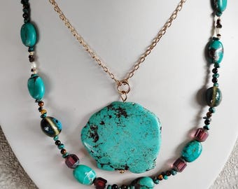 May include: A turquoise stone pendant necklace with a large, irregular shaped turquoise stone. The pendant is on a gold chain and is layered over a beaded necklace with turquoise, black, brown, and purple beads.