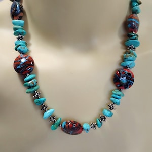 May include: A turquoise and red beaded necklace. The necklace features turquoise chip beads interspersed with larger, patterned red and black glass beads. Silver-toned metal accents are used throughout the necklace.