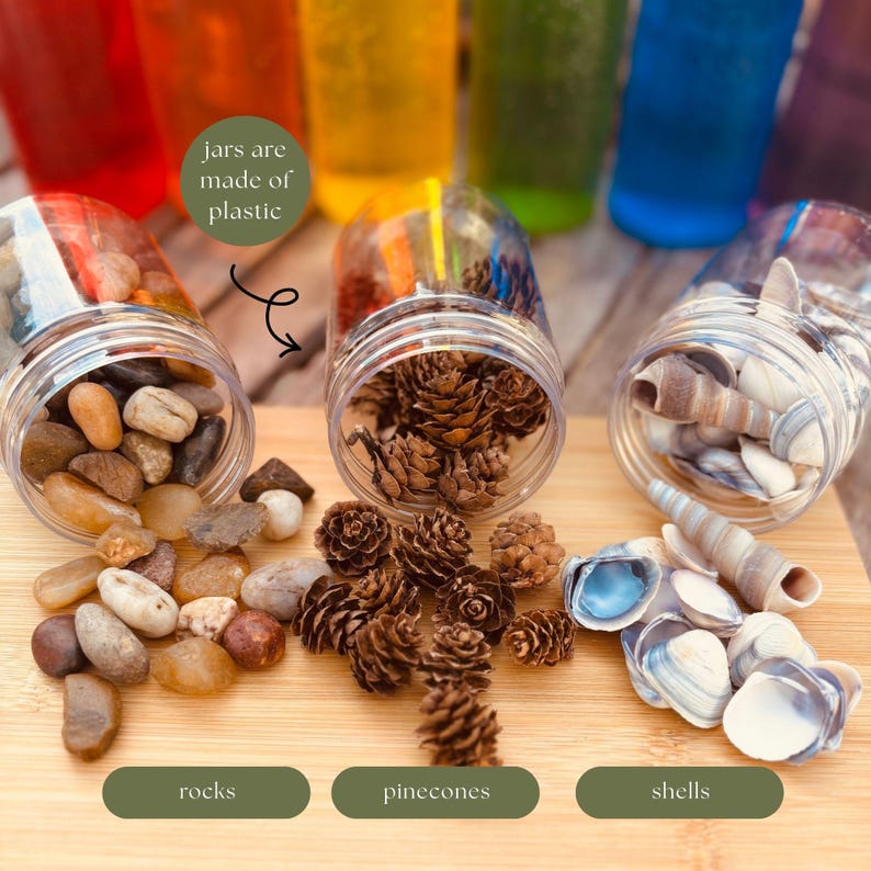 May include: Three clear plastic jars filled with natural items. One jar contains smooth, multi-colored river rocks, another holds small brown pinecones, and the third contains various white and grey seashells. Text labels read jars are made of plastic, rocks, pinecones, and shells.