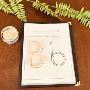 May include: A white sheet of paper with the text "I can make the letter Bb" and "Make it!"  The letter B is outlined in black and a brown playdough letter B is placed inside the outline.  The letter b is outlined in black.