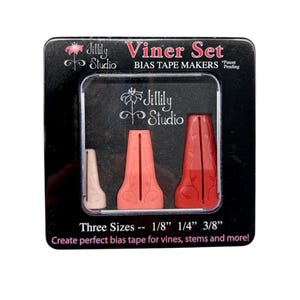May include: A Jillily Studio Viner Set containing three bias tape makers in graduated sizes of 1/8 inch, 1/4 inch, and 3/8 inch. The tools are light pink, coral, and red, featuring a vine pattern, packaged in a black box with white text.
