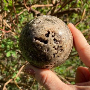 Könnte beinhalten: Eine runde, grau-braune, gefleckte Steinkugel. Die Kugel ist glatt und hat eine natürliche, organische Textur.