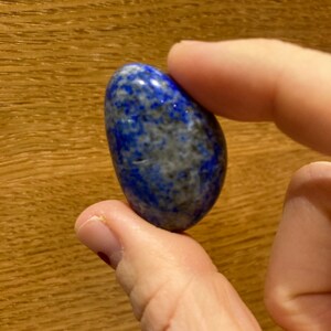 May include: A smooth, oval-shaped lapis lazuli stone with a deep blue color and white and gray marbling.