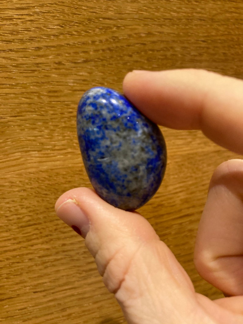 May include: A smooth, oval-shaped lapis lazuli stone with a deep blue color and white and gray marbling.